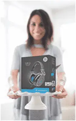 A woman stands indoors holding a white pedestal displaying a boxed pair of Sennheiser HD 280 Pro headphones.