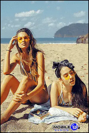 Two women relaxing on the beach with sunglasses and striped swimsuits.