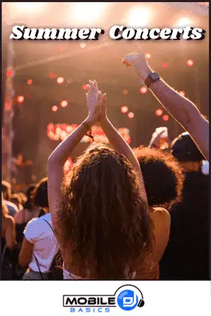Crowd enjoying summer concert with hands raised and stage lights in background.