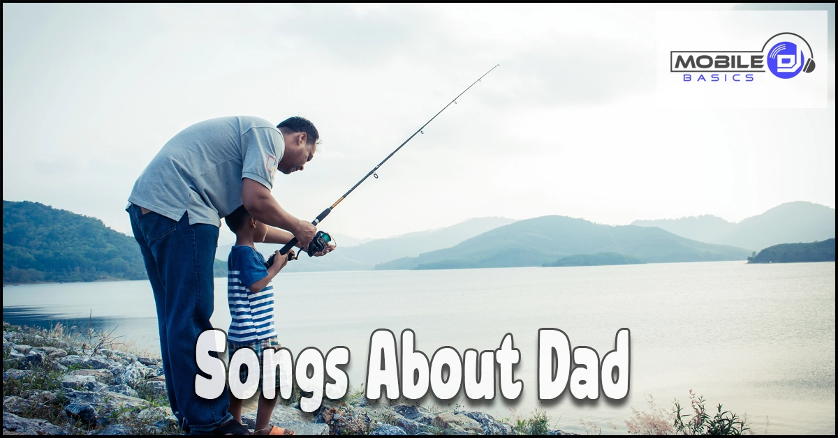 An adult and child stand on a rocky shore fishing by a lake, with hills in the background. The scene captures a peaceful moment that perfectly embodies the spirit of “Songs About Dad.” Text reads, “Songs About Dad.” Mobile Basics logo is in the top right corner.