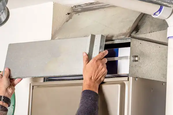 A Moore Home Services technician carefully removes the cover of a home's furnace to access and replace the air filter, ensuring your HVAC system runs efficiently and cleanly. Trust our expert team for reliable heating service—your satisfaction is always guaranteed with our clean, professional care.