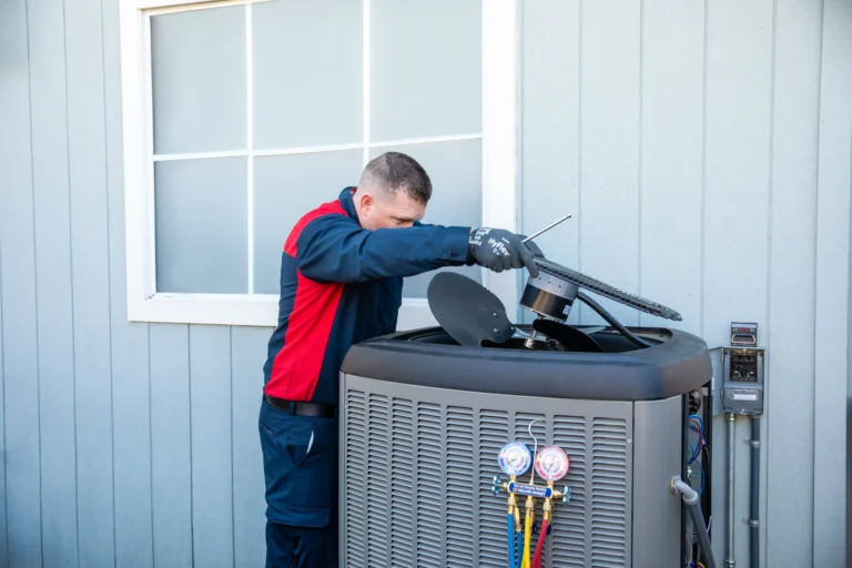 A Moore Home Services technician, dressed in our professional uniform, expertly services an outdoor air conditioning unit beside a home. With specialized tools and gauges in use, our HVAC expert ensures your cooling system runs smoothly. You can trust our team for reliable repairs and guaranteed clean service—because your comfort and satisfaction are always our top priorities.