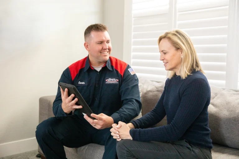 A friendly, uniformed Moore Home Services technician sits side-by-side with a homeowner, clearly explaining HVAC, plumbing, or drain solutions on a tablet. The homeowner listens attentively and confidently—trusting our expert’s advice and our industry-leading guarantees. Your comfort is always in good hands with our clean, professional service.
