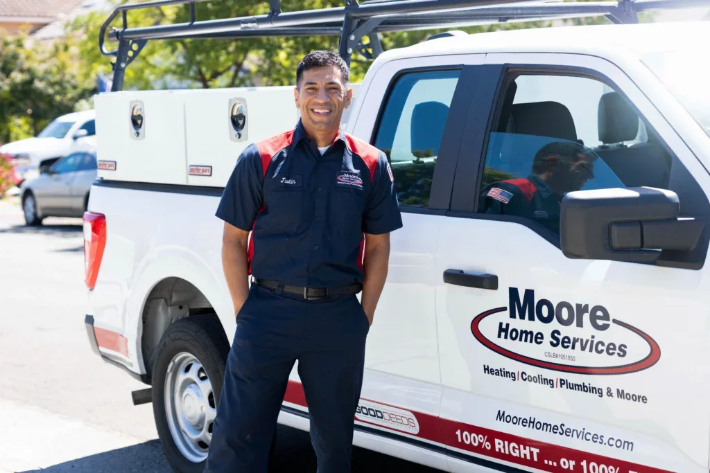 A friendly Moore Home Services technician stands by a company truck, ready to provide trusted HVAC and plumbing care—always guaranteed.