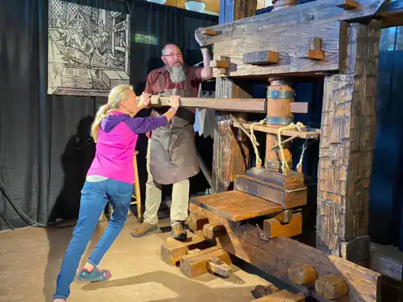 Girl and man operating a large wooden printing press at New Era Christian School.