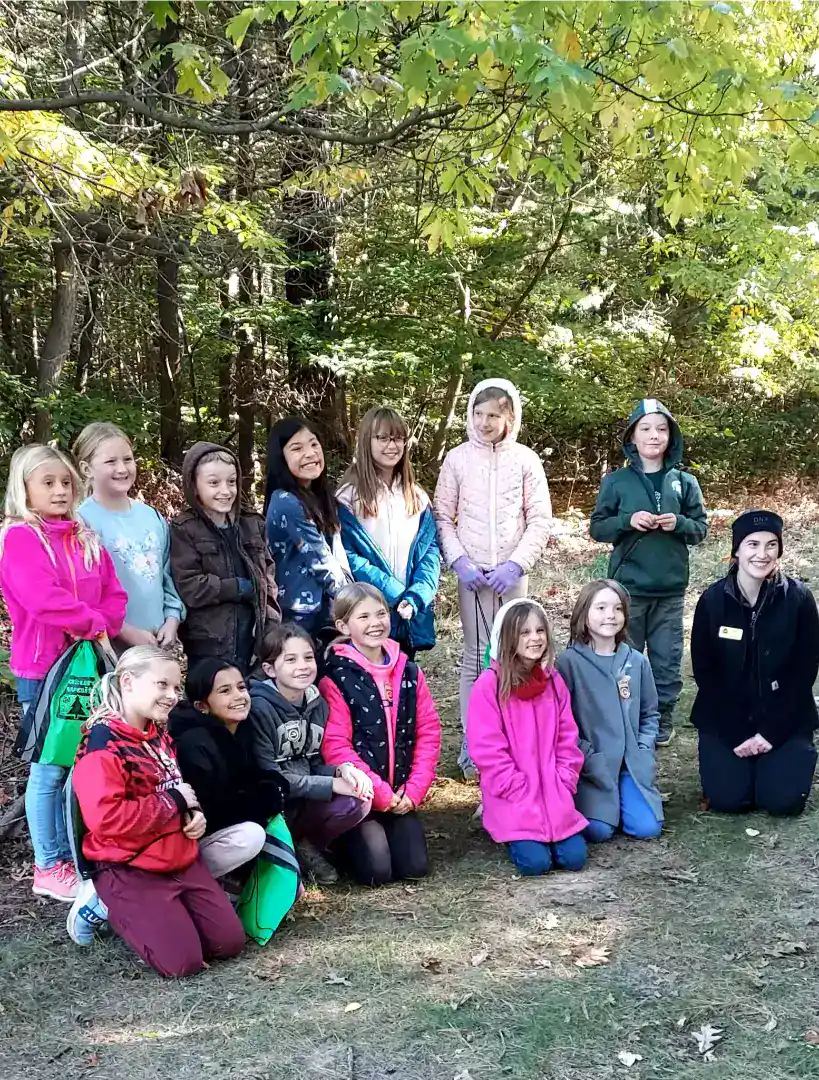 Group of children from New Era Christian School outdoors in a wooded area.