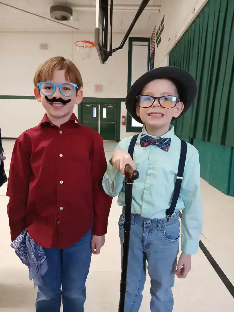 Two children in costumes at New Era Christian School, one with glasses and mustache, the other with.