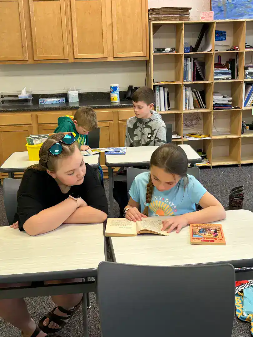 Students reading books at desks in a classroom setting.