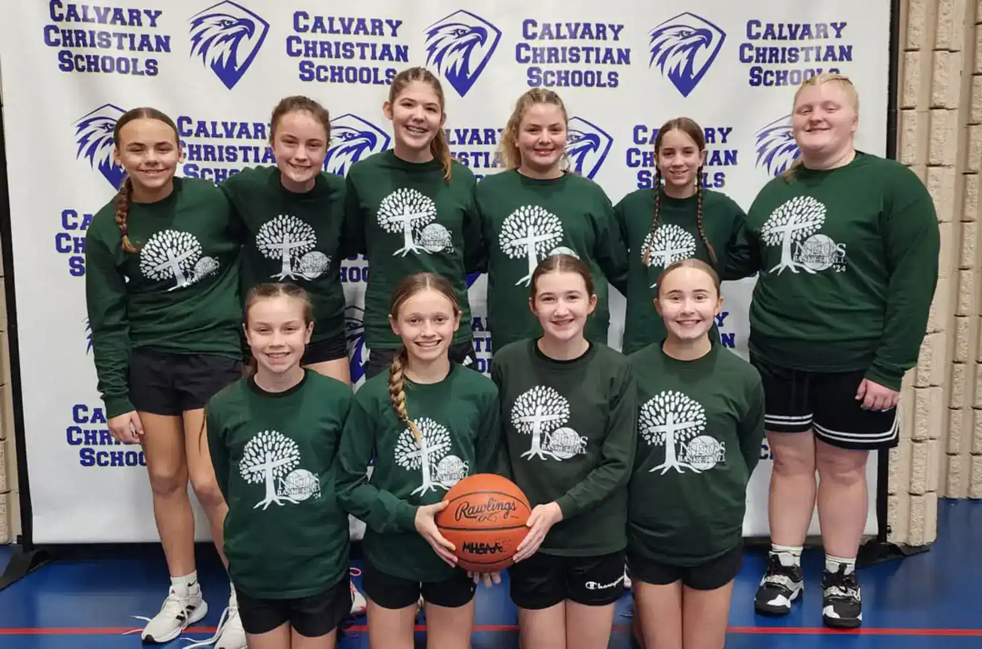 Group of young girls in green jerseys holding a basketball at school gym.