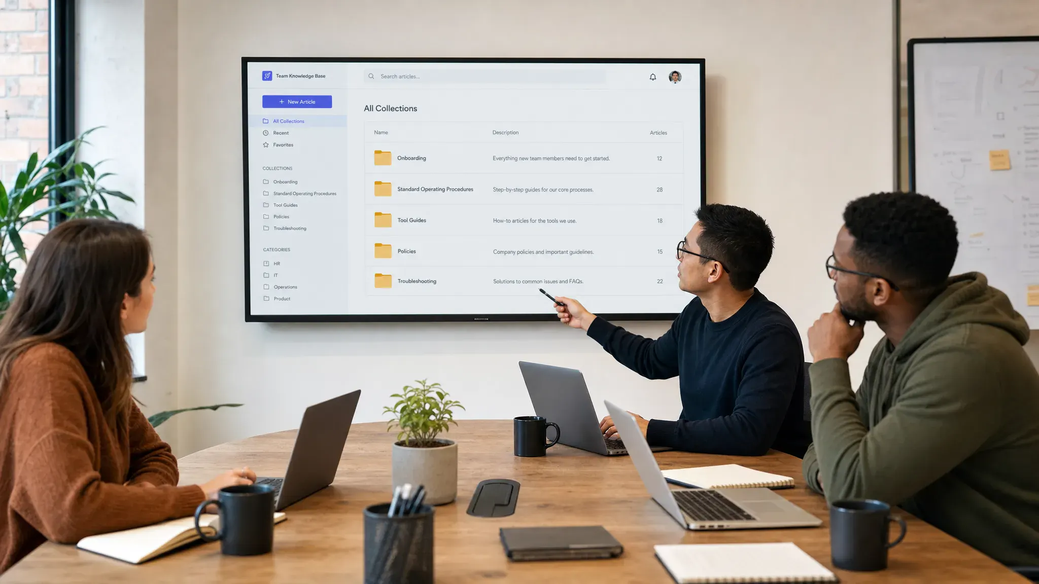 A remote team knowledge base workspace showing organized folders for onboarding, standard operating procedures, tool guides, policies, and troubleshooting articles, with teammates reviewing the structure around a shared table in an office setting.