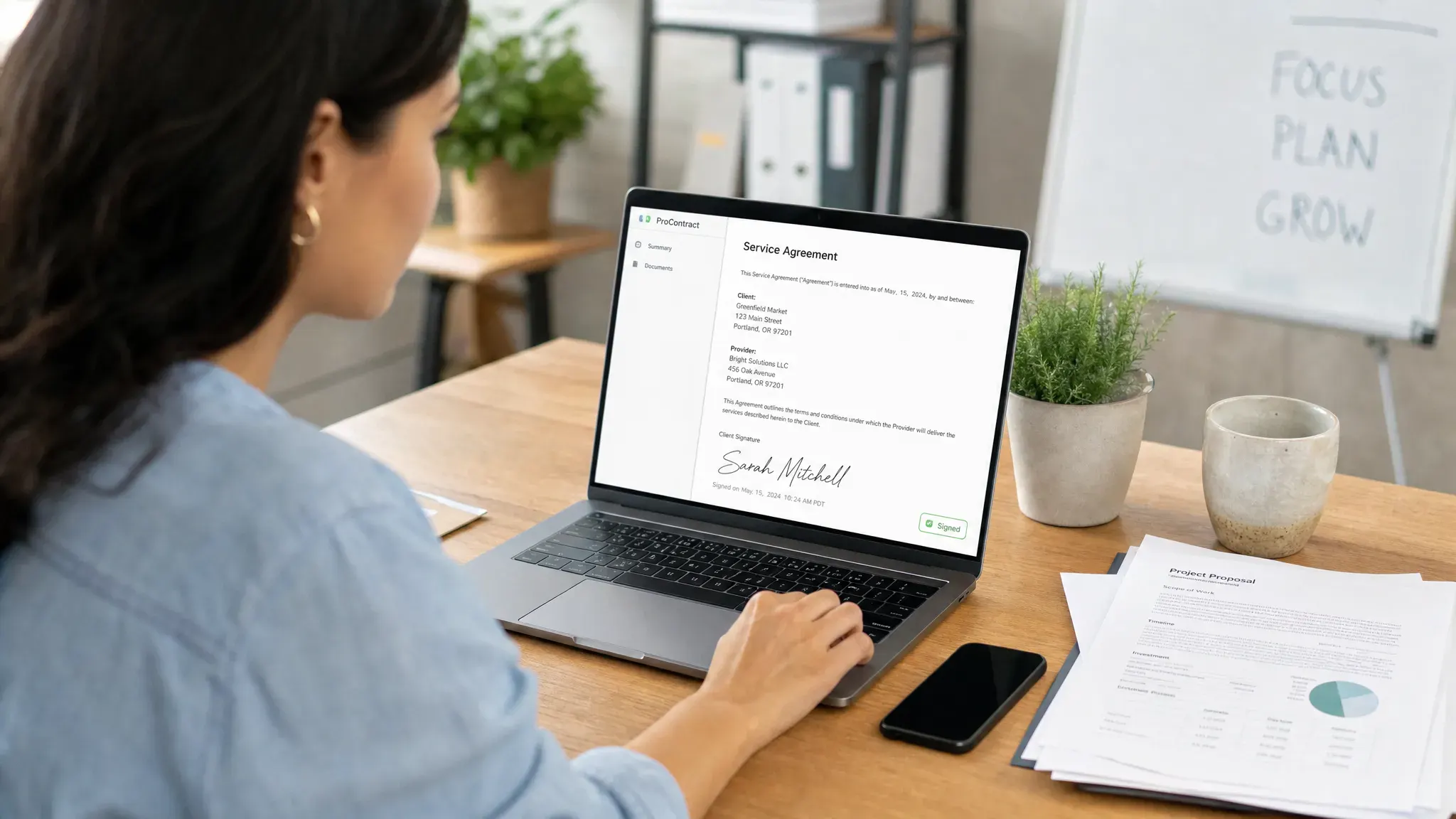 A small business owner reviewing a signed digital contract on a laptop while paper documents, a pen, and a smartphone sit neatly on the desk.