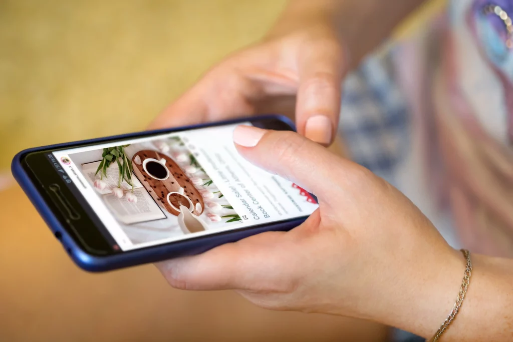 A person holds a smartphone with both hands, effortlessly browsing a recipe page designed with mobile first design, featuring a cake topped with chocolate and white icing.