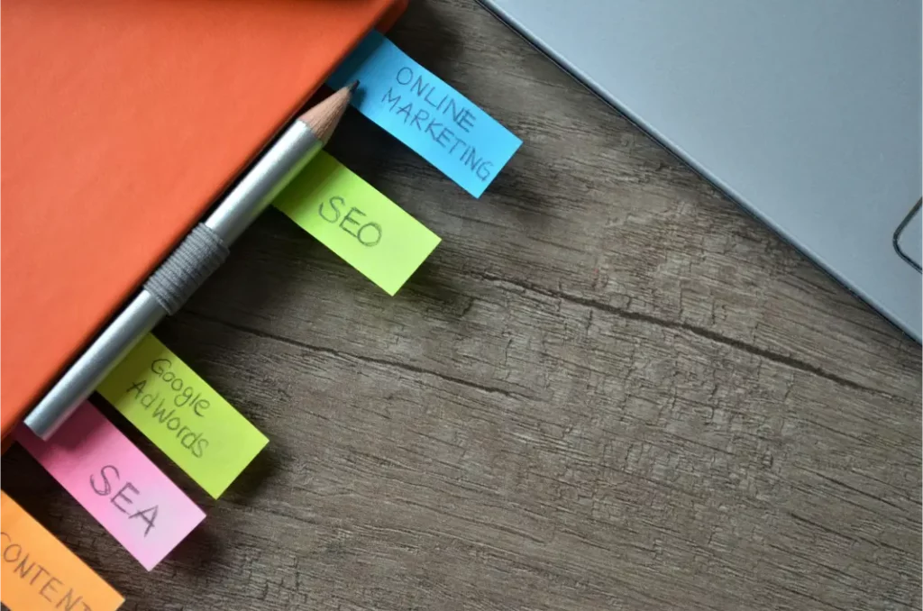 Paradox Media inbound marketing strategies. An orange notebook with tabs labeled "ONLINE MARKETING," "SEO," "Google Adwords," "SEA," and "CONTENT"—perfect for jotting down inbound marketing lead generation tips—sits beside a pencil and a laptop on a wooden desk. Paradox Media