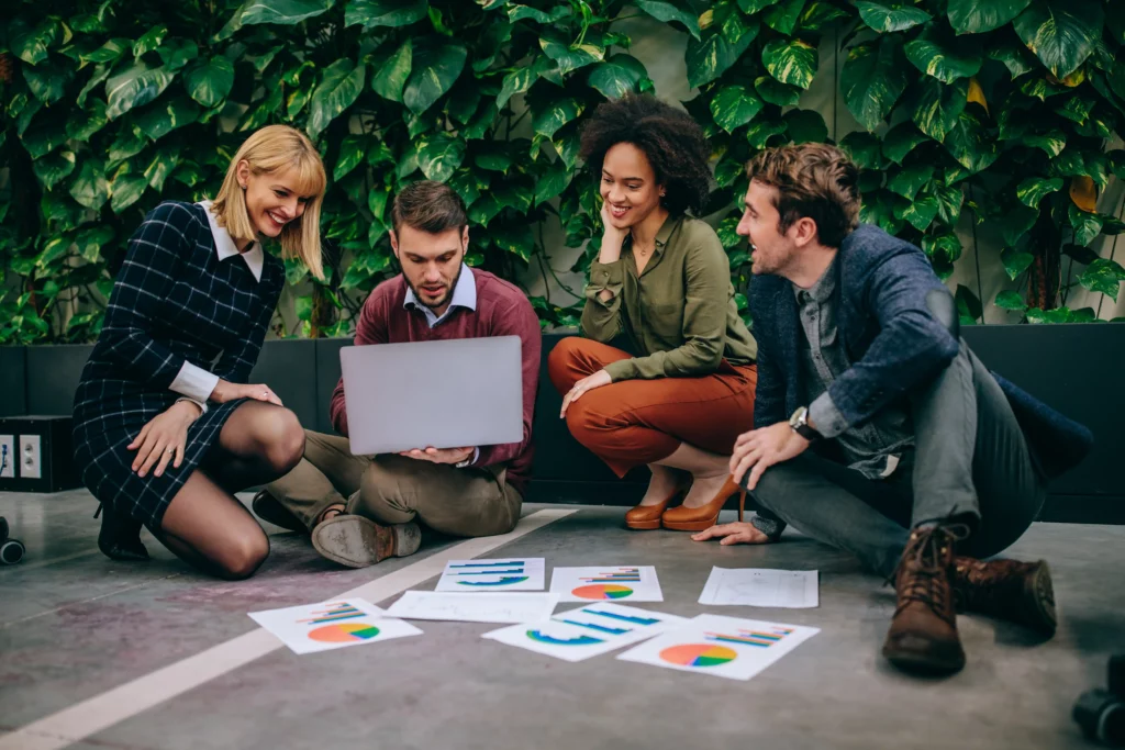 Four people sitting on a floor while surrounded by graphs and data, as they discuss local SEO content strategy and other digital marketing tasks.