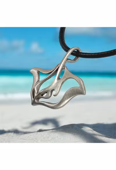 Un pendentif en forme de raie manta repose sur une plage exotique, symbolisant l'élégance et la liberté des océans. #Plongée
