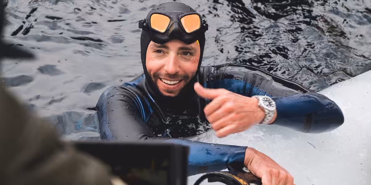 Homme en combinaison de plongée sous-marine souriant dans l'eau, explorant le monde marin.