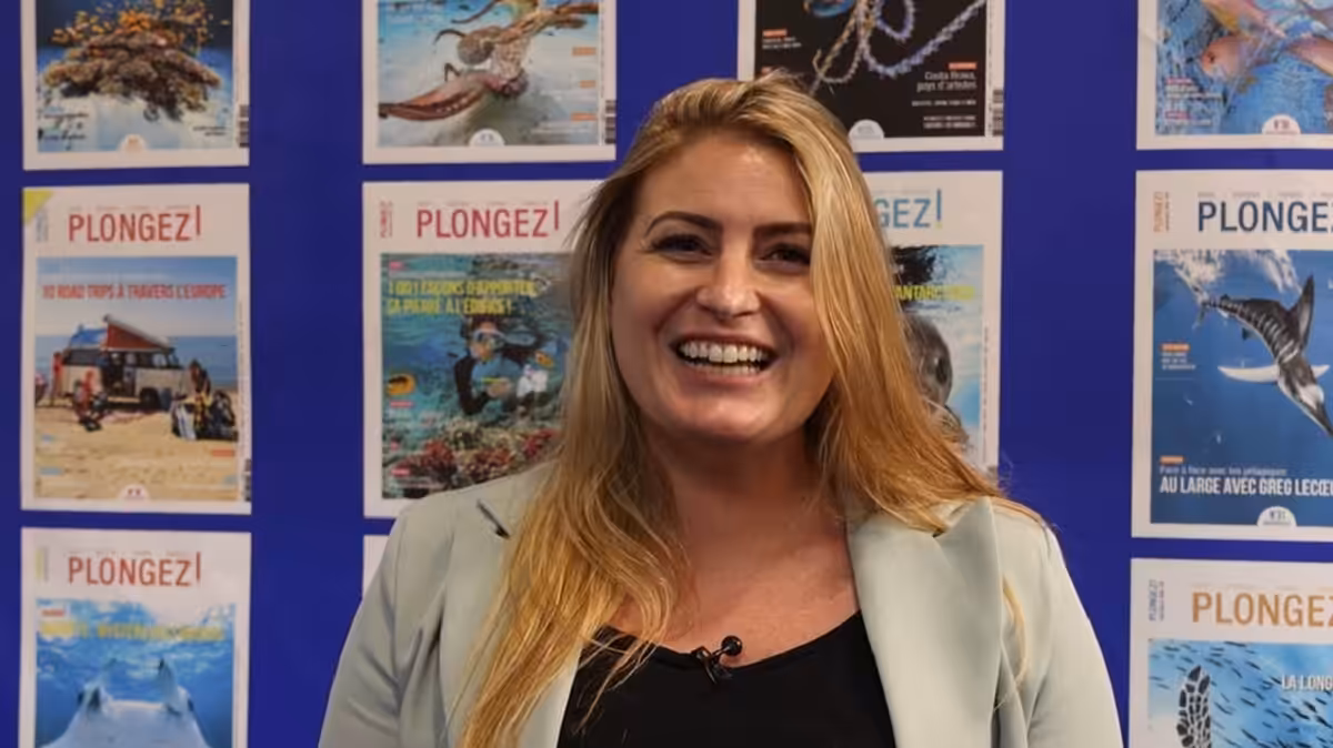Femme souriante devant des affiches sur la plongée sous-marine et la vie marine.