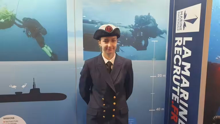 Femme en uniforme naval devant un stand sur les missions sous-marines et la Marine Nationale.