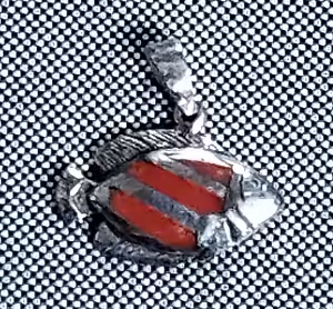 Un pendentif en forme de poisson, évoquant l'exploration marine, repose sur un fond texturé, symbole d'aventure sous-marine.