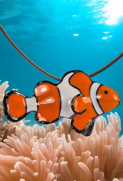 Un pendentif en forme de poisson-clown flotte au-dessus d'une anémone, évoquant l'éclat coloré des récifs coralliens.