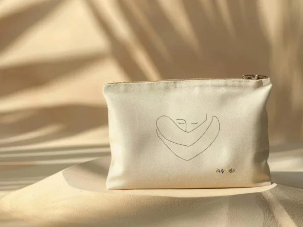 pochette-pochi-confiance-en-soi Pochette Pochi Confiance en soi avec un tracé représentant une personne qui se prend elle-même dans ses bras, logo Pochi Kibo en bas à droite, posée sur un dôme de sable avec fond beige assorti et ombres végétales, ambiance naturelle et douce.