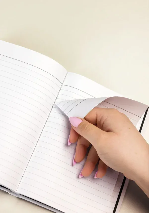 Hand turning a lined page inside the journal, showing the perforated tear-out edge.