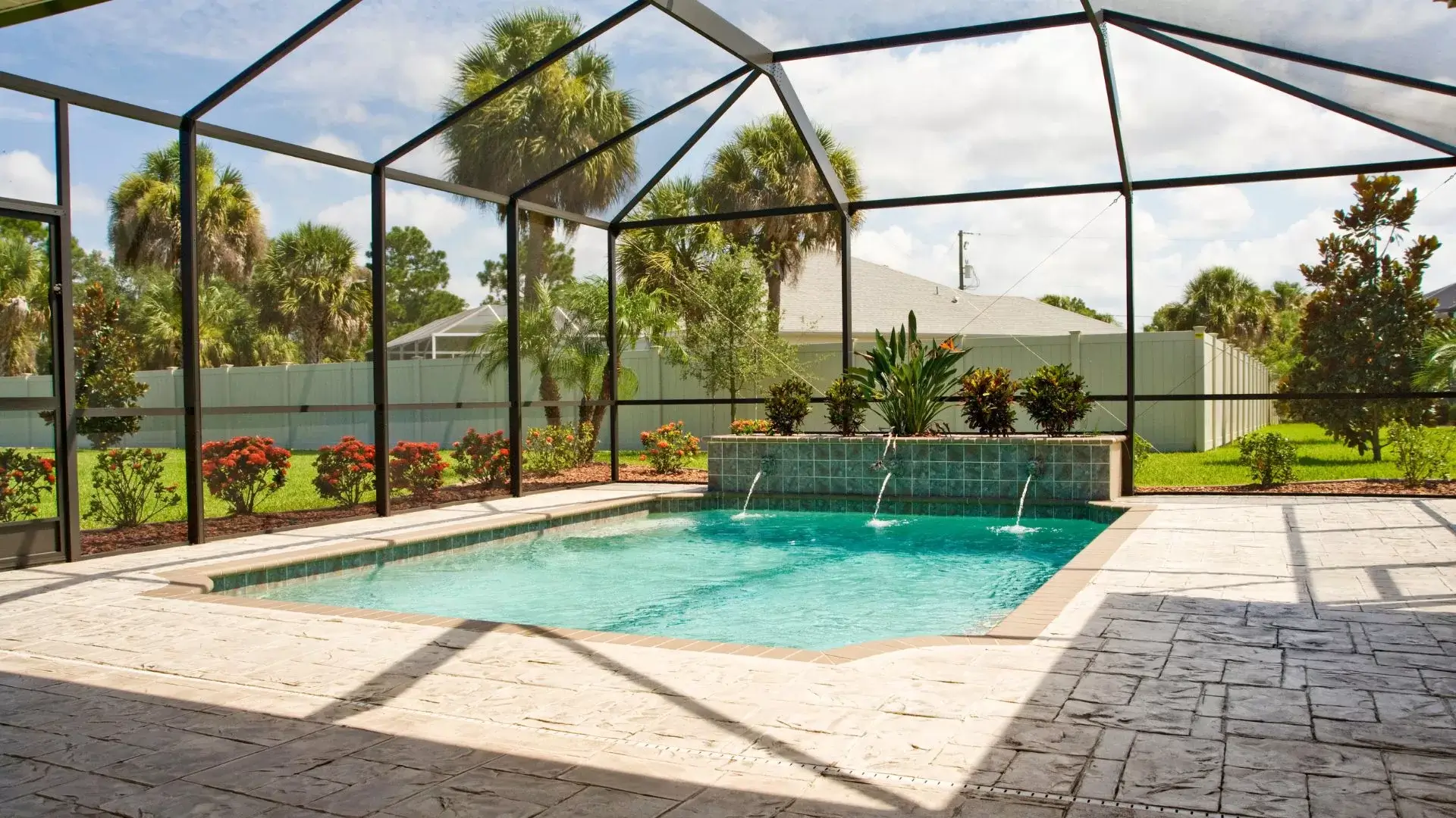 A beautiful screen enclosures cover a pool surrounded by a stone patio and beautiful landscaping.