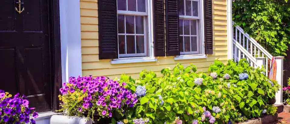 Yellow house with black shutters and colorful flower garden in West Michigan.