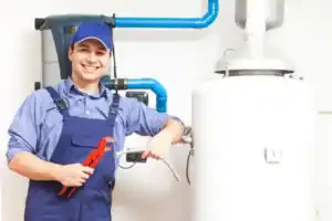 A friendly plumber in blue overalls stands by a water heater, ready to help Southern California homeowners with trusted service.