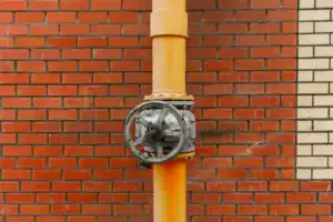 A sturdy yellow metal pipe with a secure valve wheel is installed along a red and white brick wall, ensuring reliable home service.