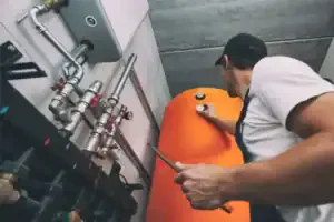 A Service Champions technician carefully adjusts valves on an orange water heater, ensuring reliable home comfort for local families.
