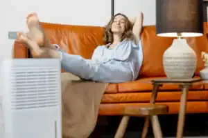A woman relaxes on a brown leather sofa near a lamp and air comfort unit, enjoying dependable home comfort in her living room.