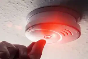A caring hand tests a ceiling-mounted smoke detector, red light glowing—your safety is our top priority at Service Champions.