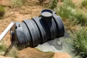 A durable black septic tank with white inlet pipe is installed in your yard, ensuring reliable service from your local experts.