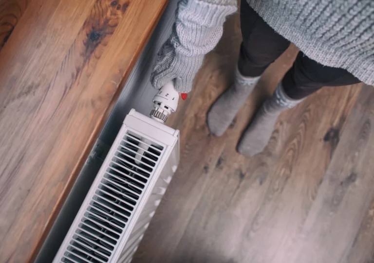 A customer in cozy wool socks and gloves adjusts a heater dial, trusting a local expert to ensure warmth and comfort at home.