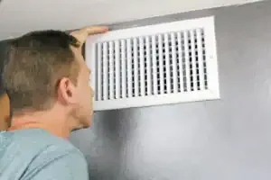A friendly Service Champions technician inspects a white air vent after expert air duct installation in a Brea, CA home.