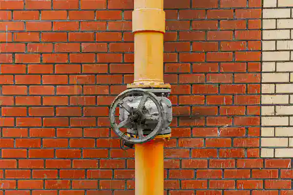 A yellow gas line pipe and sturdy metal valve wheel stand out on a red brick wall, ready for trusted gas line repair in Brea, CA.