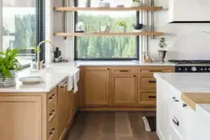 Inviting Brea kitchen with light wood cabinets, white counters, open shelving, forest view window, and reliable plumbing fixtures.
