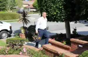 A friendly Service Champions technician approaches a Brea home, ready to help, with a service van nearby and lush landscaping.