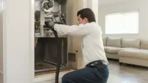 A friendly Service Champions technician carefully vacuums a wall-mounted furnace in a Brea home, ensuring reliable comfort.