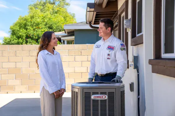 A friendly Service Champions technician explains CHAMP-Rewards benefits to a homeowner by her AC unit, ensuring trusted comfort.