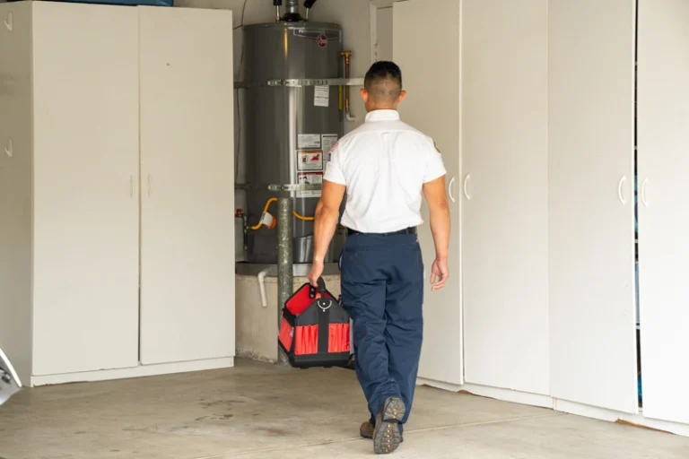 A trusted expert with a red and black tool bag heads to install a water heater in a Brea, CA garage, ready to help your home.