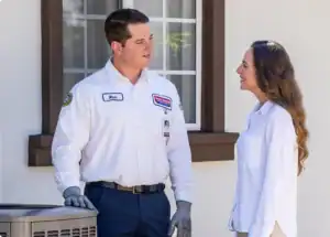 A friendly Service Champions technician chats with a homeowner beside an HVAC unit, providing trusted, expert home comfort advice.