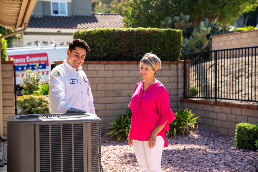 A friendly Service Champions technician inspects an AC unit in a sunny yard, ensuring trusted comfort for a local Southern CA family.