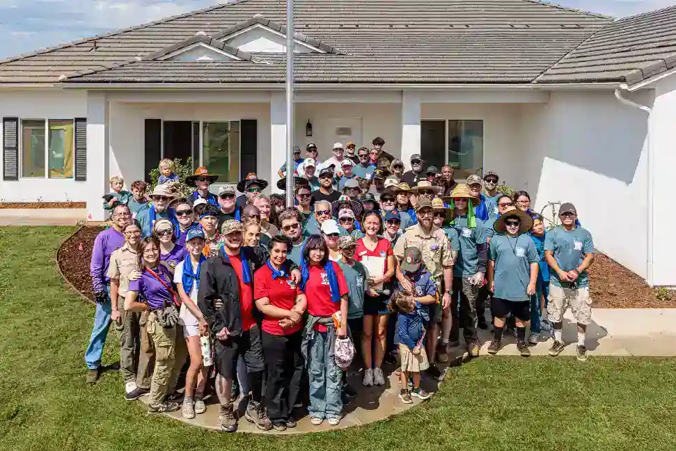 A dedicated group of community members, including veterans, gather with friendly smiles outside a well-kept white home on a sunny lawn, dressed in comfortable attire that reflects their helpful spirit. Their camaraderie showcases the reliable, customer-focused service that Service Champions brings to Southern California homeowners seeking trusted HVAC, plumbing, and drain solutions.