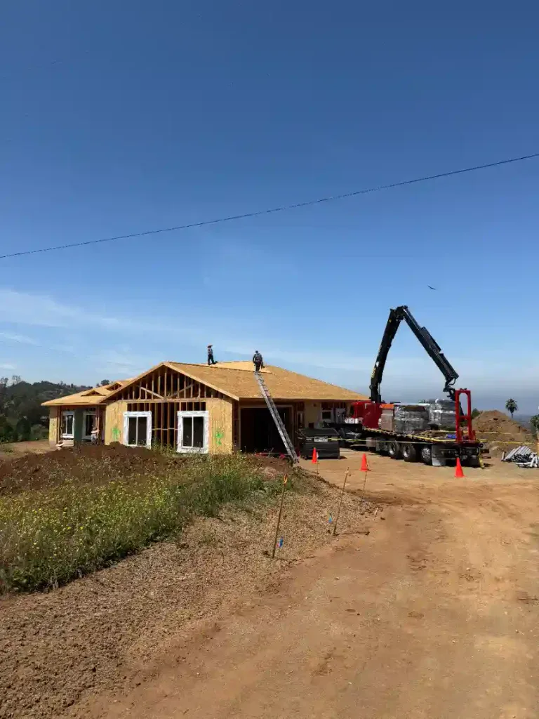 A single-story home is under construction, with dedicated workers on the roof and a crane truck carefully lifting materials nearby. Surrounded by open dirt and sparse greenery, Service Champions brings dependable home comfort expertise to this project, working alongside Homes For Our Troops to create a welcoming space for veterans. As your trusted local HVAC, plumbing, and drain professionals in Southern California, Service Champions demonstrates their ongoing commitment to helpful service and genuine care for the community.