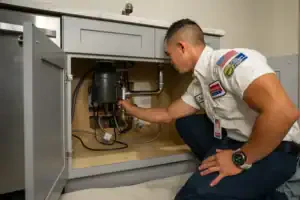 A trusted Service Champions plumber inspects pipes and disposal under a kitchen sink, ensuring reliable, expert drain care for your home.