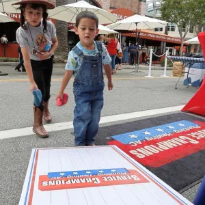 Two young children play bean bag toss on a vibrant Southern California street, reflecting our dedication to local family comfort.