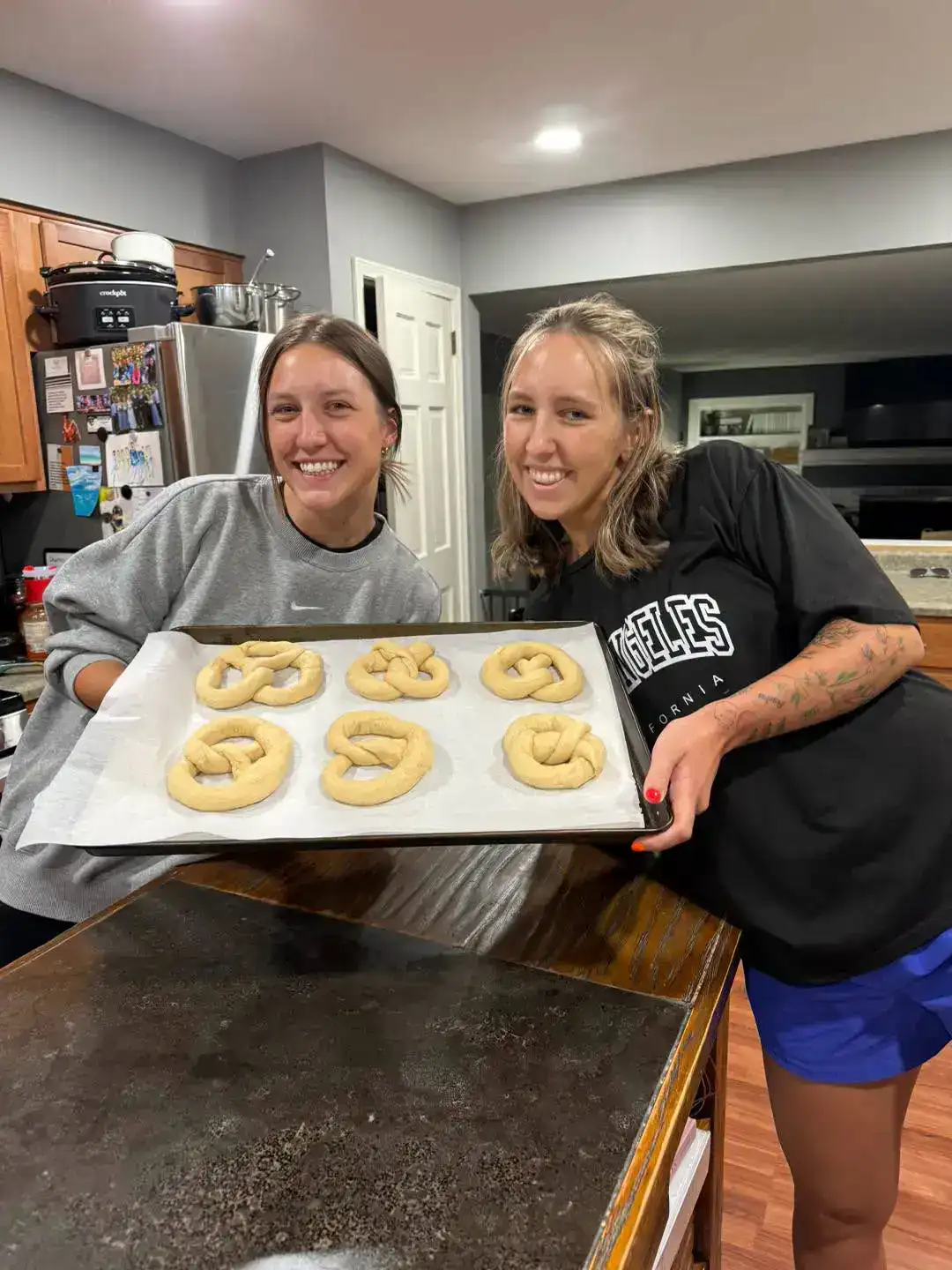 Two women holding a tray of freshly baked pretzels in the bakery kitchen.
