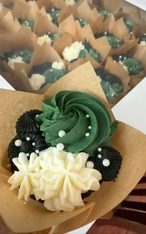 Decorative cupcake with green, black, and white frosting and pearl sprinkles.